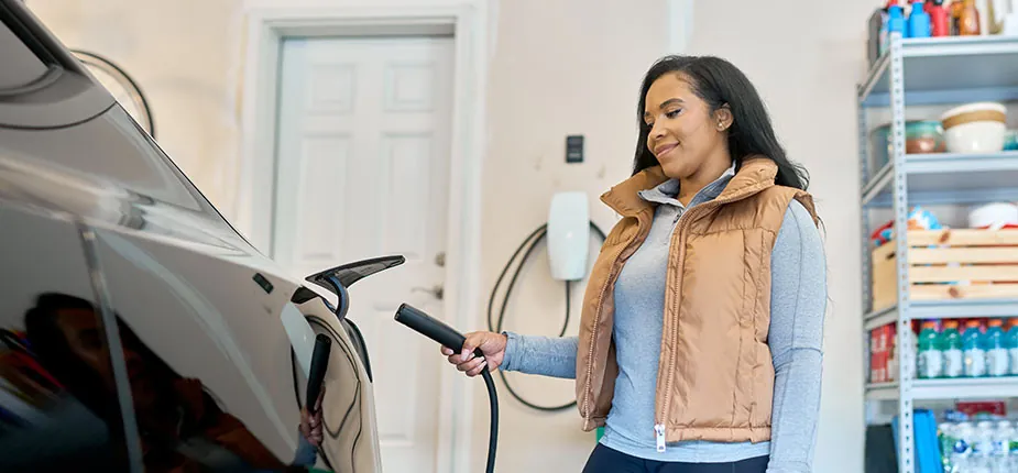 Woman plugging an electric car into a wall charger in her home garage